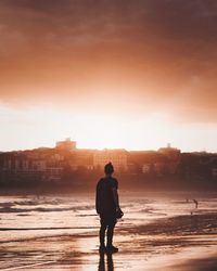 Man standing on shore at beach during sunset