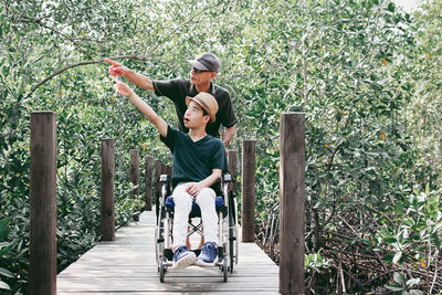 Father with disabled boy on wheelchair against trees