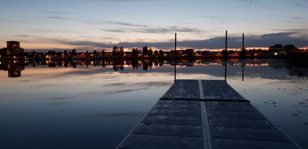 Scenic view of river by illuminated city against sky at sunset