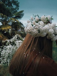 Rear view of woman with flowers against sky