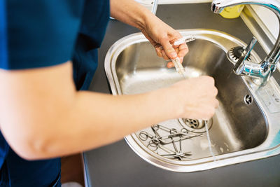 From above anonymous doctor washing vials and scissors over sink during work in hospital