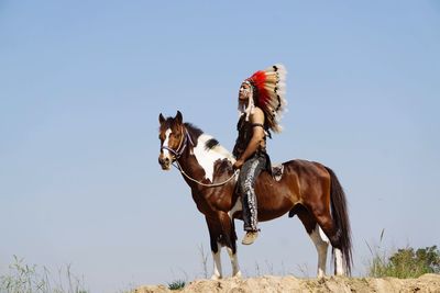 Man horseback riding on field against clear sky during sunny day