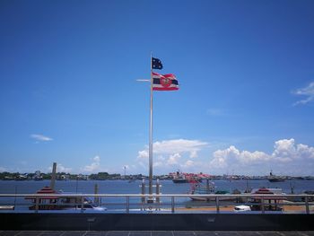 Flag on pole by sea against blue sky