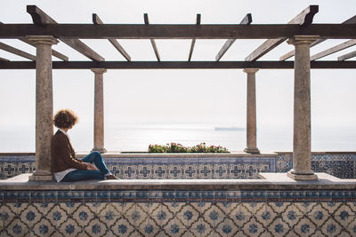 Woman sitting on built structure in city