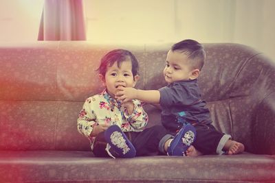 Cute siblings sitting on sofa at home