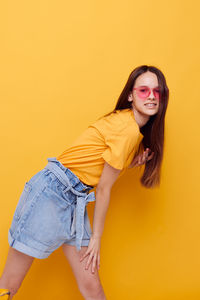 Portrait of teenager girl standing against yellow background