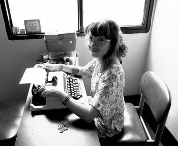 Portrait of woman using vintage typewriter while sitting by window