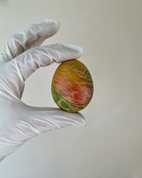 Cropped hand of person holding easter egg against white background-wall.