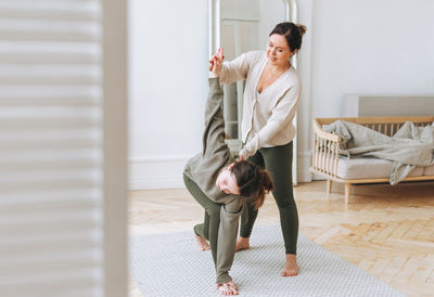 Attractive mother middle age woman and daughter teenager ptactice yoga together in the bright room