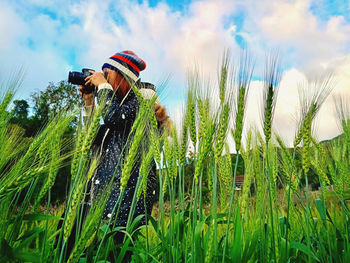 Man photographing amidst grass against sky