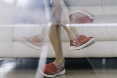 Low section of man sitting on sofa with reflection over glass