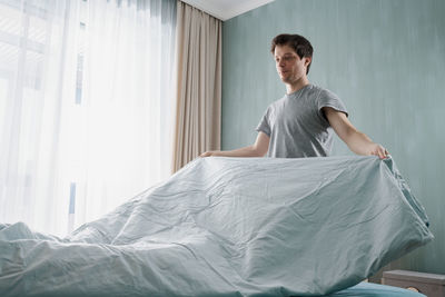 Adult man is putting the bedding cover or mattress pad on the bed. regular bed linen change