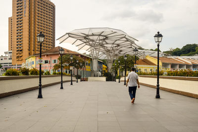 Rear view of man walking on footpath by buildings against sky