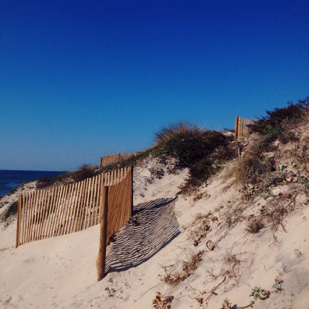 clear sky, beach, sand, copy space, blue, sea, built structure, tranquility, shore, sunlight, tranquil scene, horizon over water, architecture, absence, wood - material, nature, day, shadow, outdoors, water