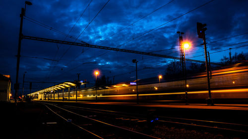 Railroad tracks on illuminated street against sky at night