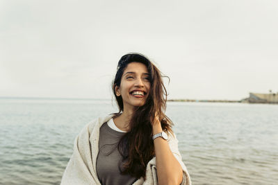 Portrait of smiling young woman standing in sea against sky