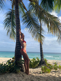 Young woman on palm tree at beach against sky