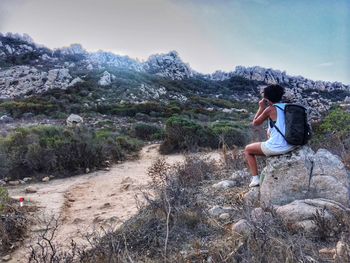 Side view of woman with backpack sitting on rock