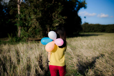 Rear view of woman holding balloons on field