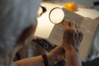 Senior woman with magnifying glass reading book at home