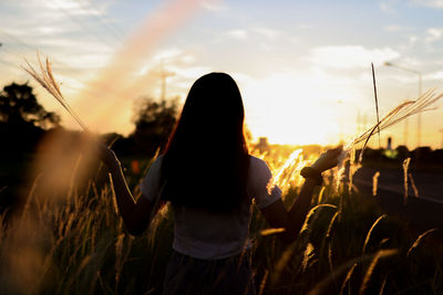 Rear view of woman standing on field against sky during sunset