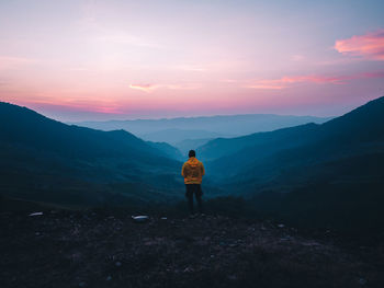 Rear view of man standing on mountain against sky