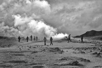 People on volcanic landscape against cloudy sky