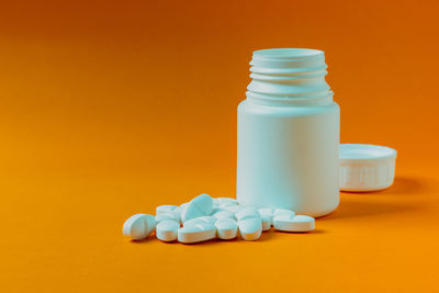 Close-up of pills spilling from bottle against yellow background