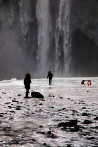 People standing in water against waterfall