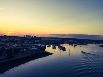 Scenic view of river by buildings against sky during sunset