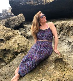 Full length of woman wearing sunglasses while sitting on rock