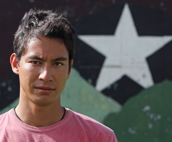 Young eurasian adult looking into the camera with a serious look in front of a wall with a star.