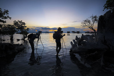 Silhouette man and woman photographing sea during sunset