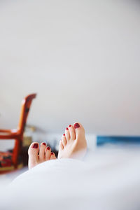 Low section of woman relaxing on bed against wall at home