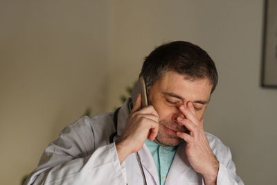 Close-up of mature doctor using phone against wall