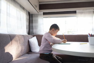 6-year-old caucasian boy paints inside caravan on weekend trip.