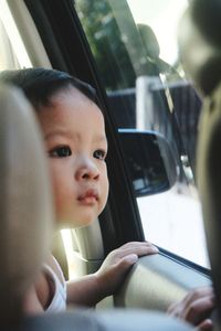 Close-up of cute baby boy looking through window in car