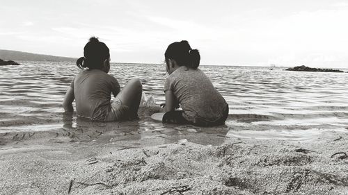 Rear view of siblings sitting at beach 