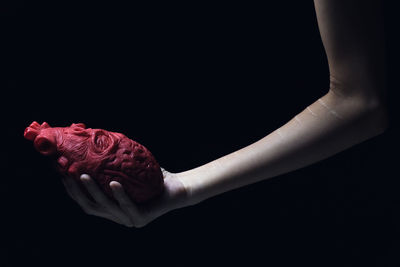 Close-up of hand holding red heart over black background