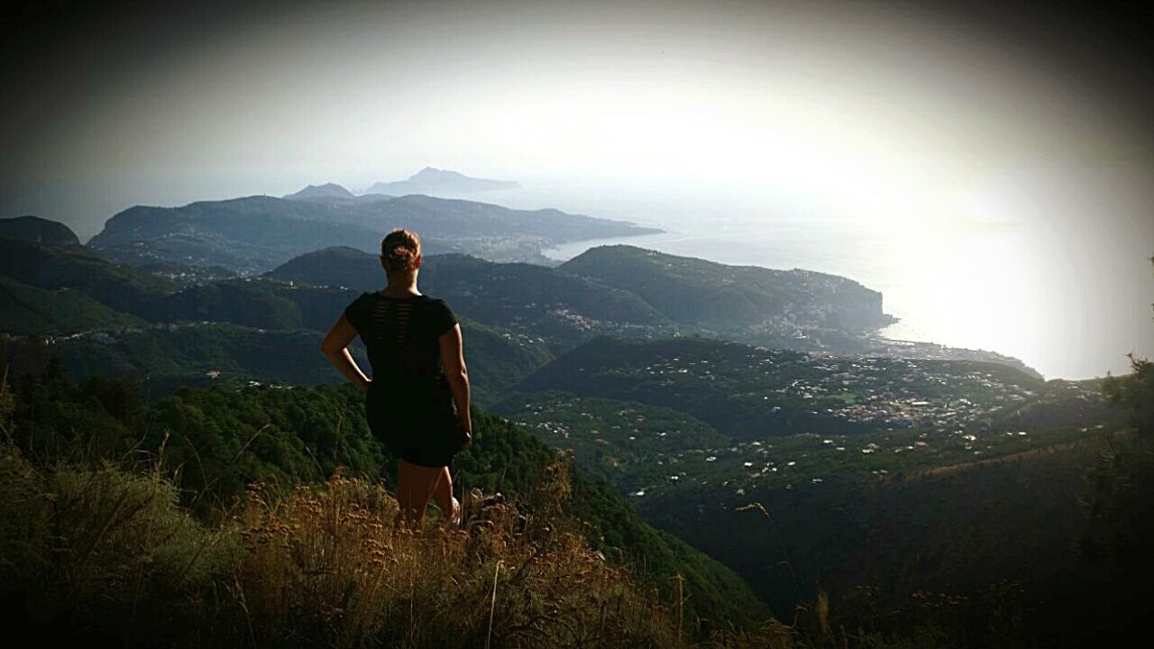 mountain, men, rear view, standing, tranquil scene, mountain range, scenics, tranquility, leisure activity, beauty in nature, non-urban scene, nature, sky, remote, mountain peak, day, sunbeam, outdoors, physical geography, lens flare