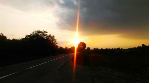 Road amidst silhouette trees against sky during sunset