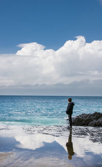 Side view of boy standing on beach against sky during sunny day