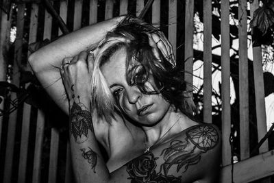 Portrait of shirtless woman with tattoos standing against fence