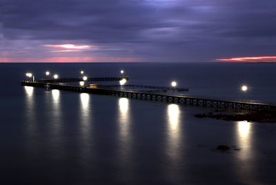 Illuminated bridge over sea against sky at night