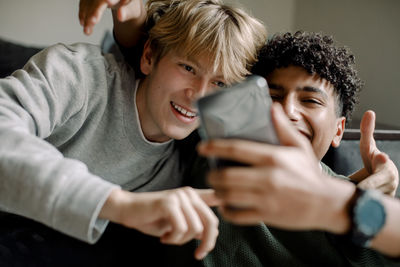 Smiling teenage boys taking selfie with smart phone at home