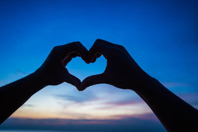 Close-up of hand making heart shape against sky during sunset