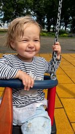 Happy toddler sitting in a swing at the playground