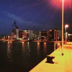 Illuminated buildings by river against sky in city at night