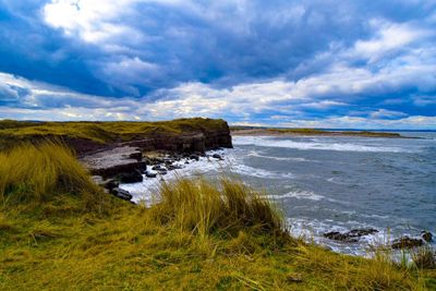 Scenic view of sea by mountain against cloudy sky