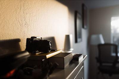 Professional photo camera illuminated by sunlight placed on wooden chest of drawers in room with contemporary interior